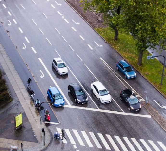 Regnvåd vej i Aarhus med biler, der holder og venter ved et vejkryds.