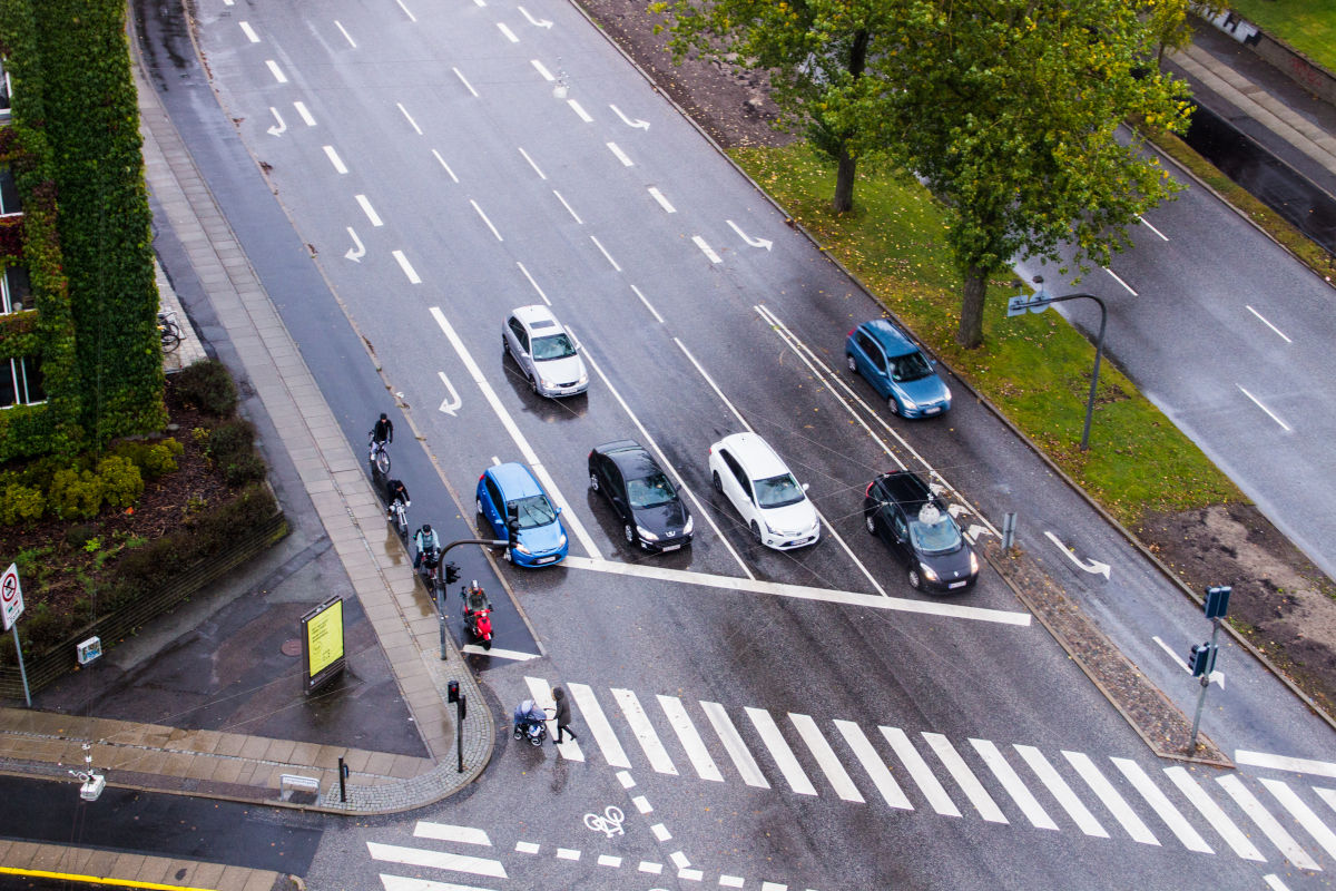 Regnvåd vej i Aarhus med biler, der holder og venter ved et vejkryds.
